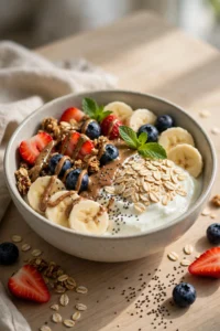High-protein breakfast bowl with Greek yogurt, oats, banana slices, blueberries, strawberries, almond butter and granola